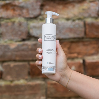 Hand holding a bottle of Katherine Danieli product against a brick wall.